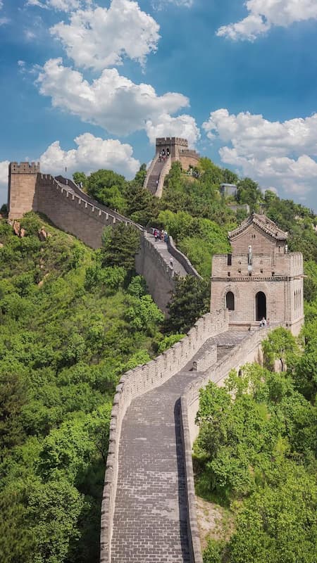 Badaling-Great-Wall-Beijing-Panoramic-View Scenic panoramic view of the ancient Badaling Great Wall in Beijing, China, showcasing its majestic stone structure winding through lush green mountains under a blue sky.
